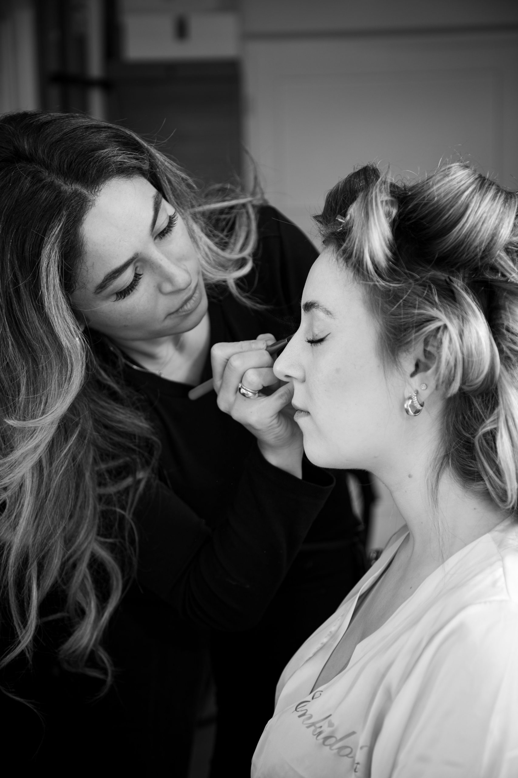 Black and white portrait of a makeup artist applying cosmetics to a client in a salon setting.
