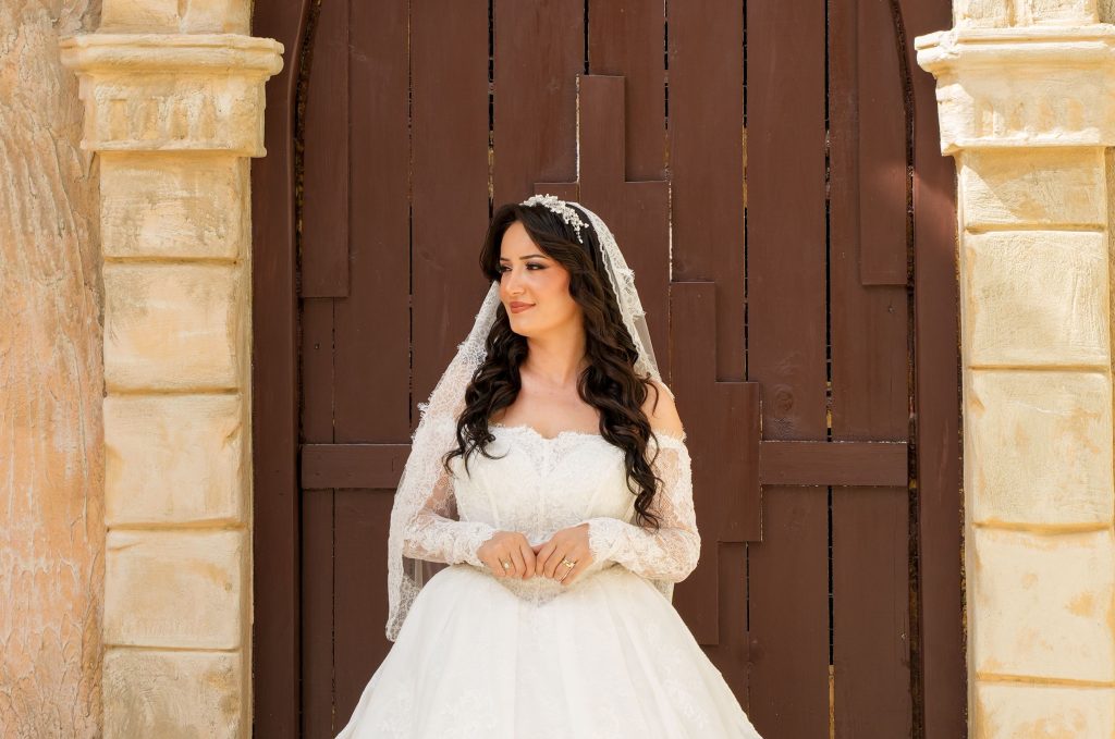 Beautiful bride posing in a lace gown outdoors with a wooden door backdrop.